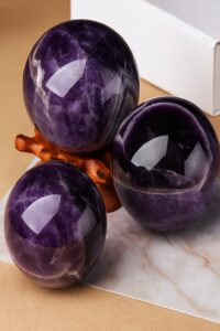 Three polished amethyst spheres of varying sizes resting on a wooden stand against a neutral background.